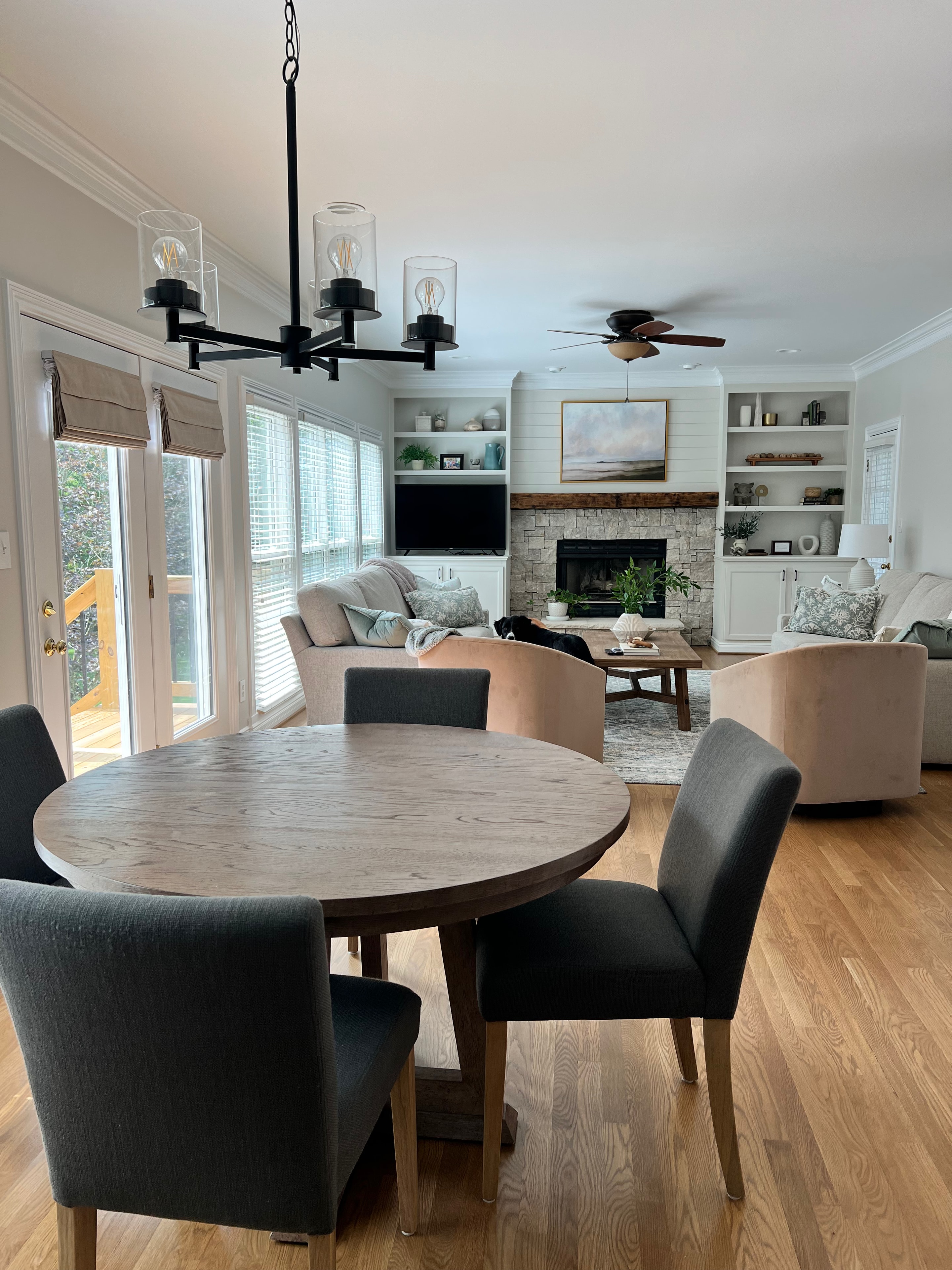 Living Room & Kitchen remodel — dining area with round table and black chandelier looking into living room with stone fireplace and built-ins by Luxe Built Louisville KY