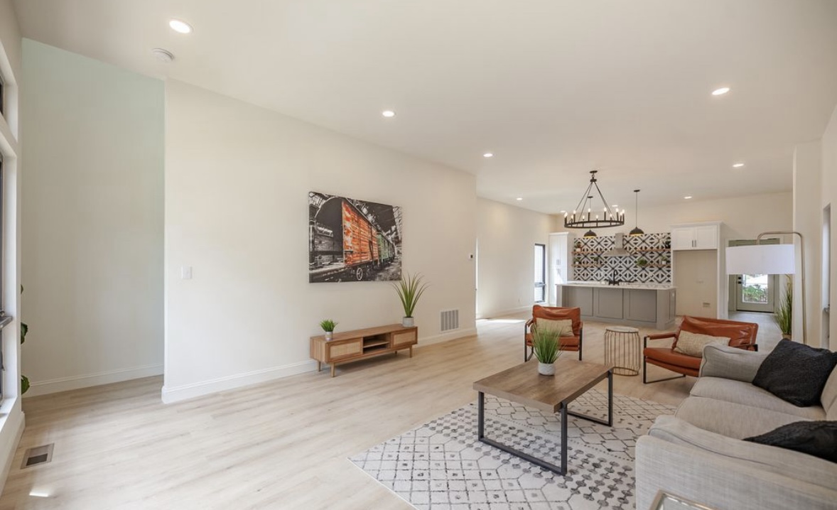 The Narrow House — open-plan living room looking toward kitchen with leather chairs, chandelier, and light hardwood floors by Luxe Built Louisville KY