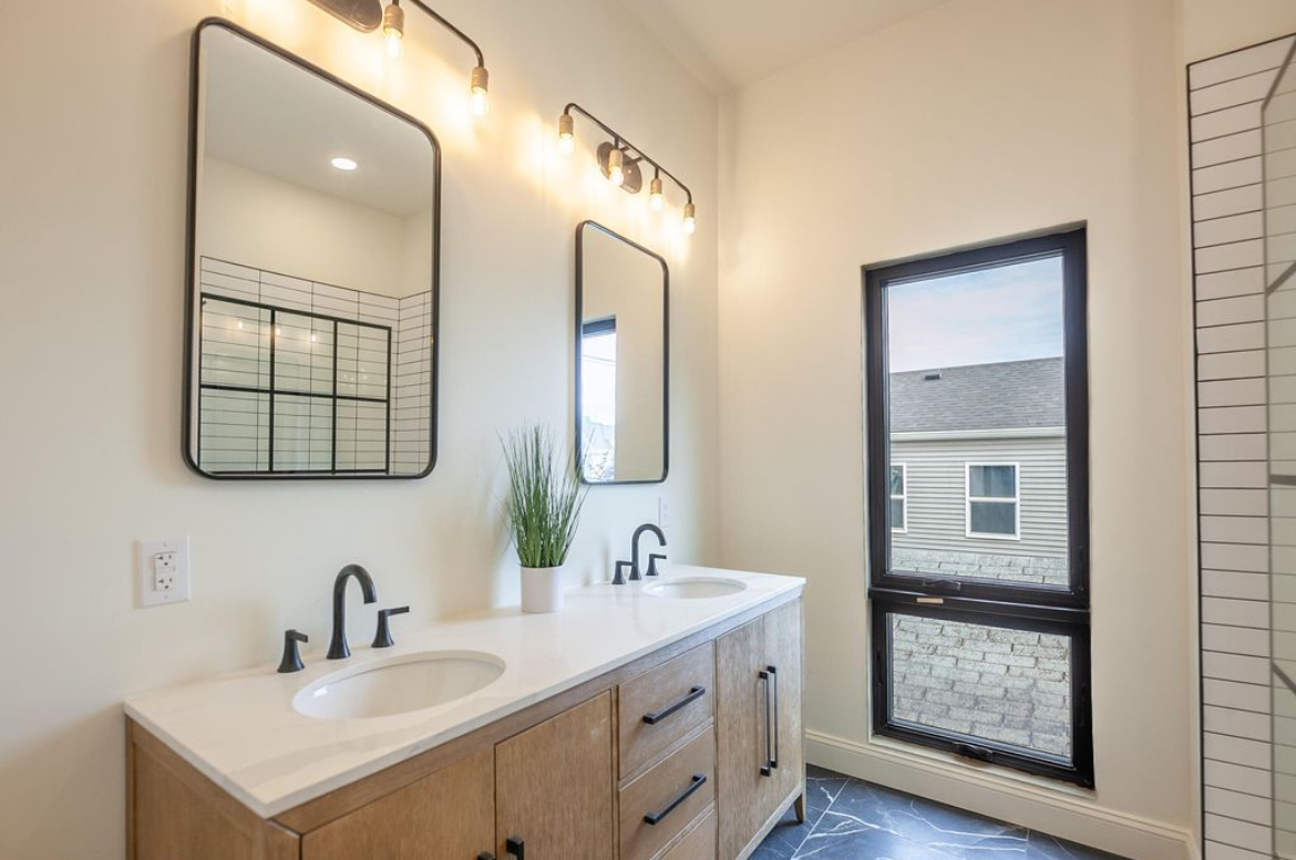 The Narrow House — primary bathroom with double vanity, warm oak cabinetry, black-frame mirrors, and walk-in shower by Luxe Built Louisville KY